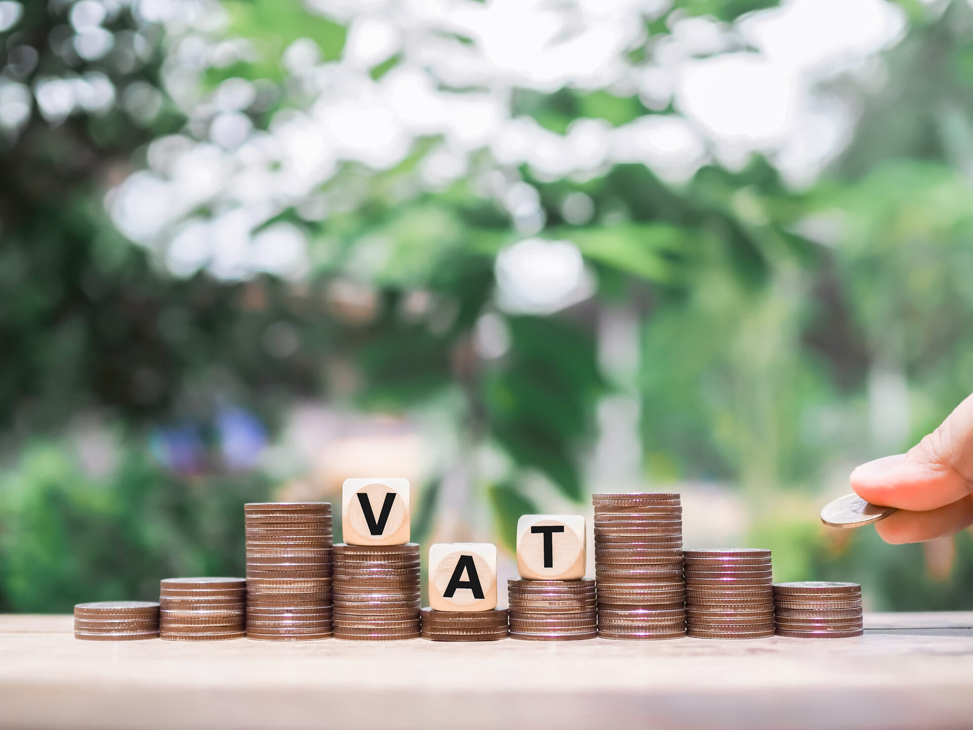vecteezy_close-up-hand-putting-coin-in-stack-of-coins-wooden-blocks_30534680